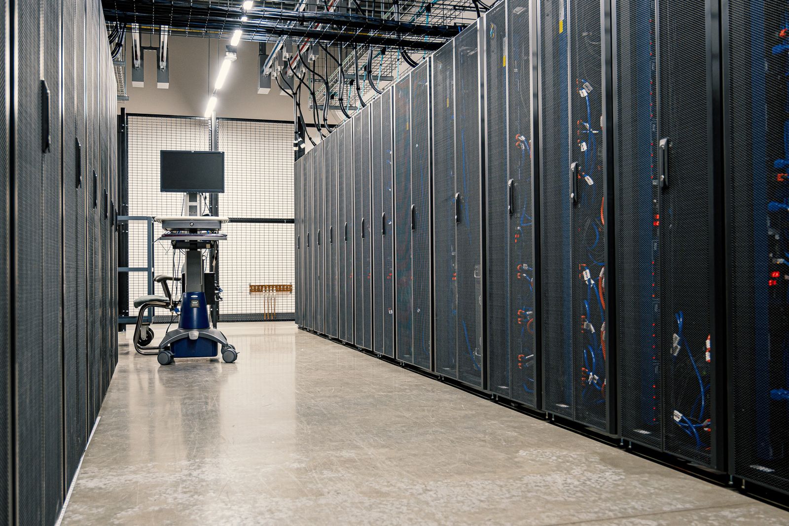 A corridor of server racks in a modern data centre, representing the systems and certificates a cryptographic inventory has to account for.