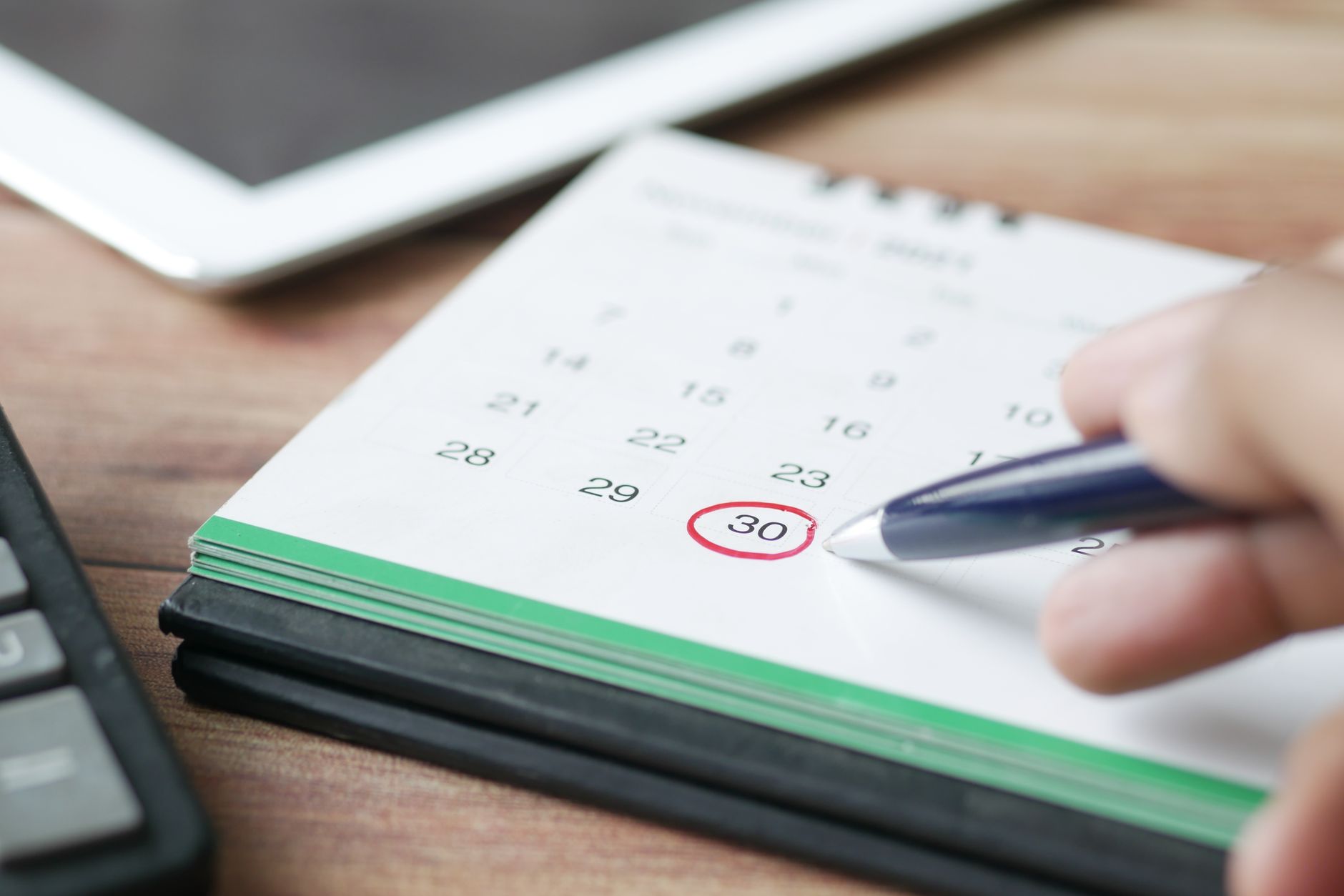A hand holding a pen circles a date on a desk calendar.
