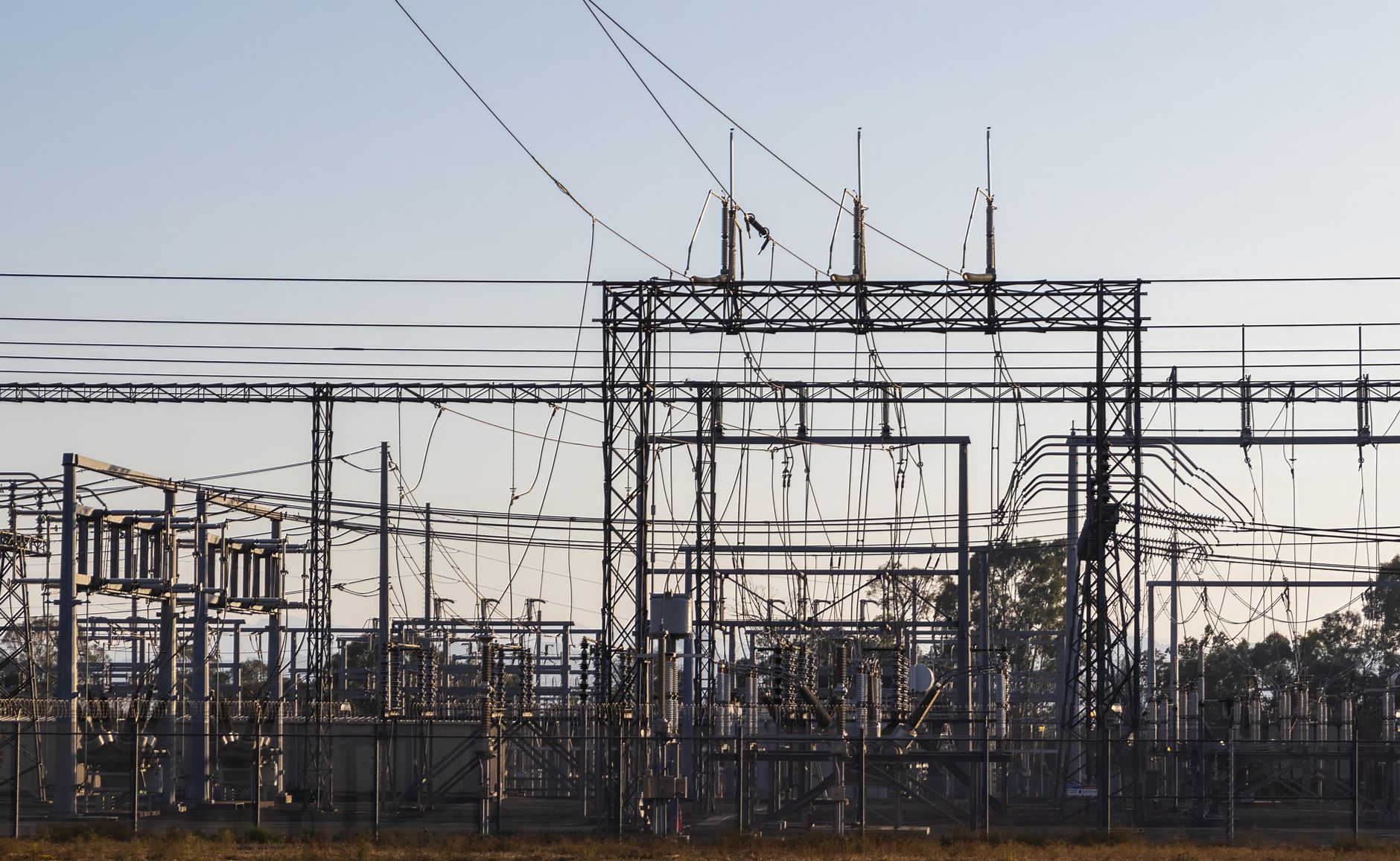 A high-voltage electrical substation with steel gantries and power lines against a pale dawn sky.