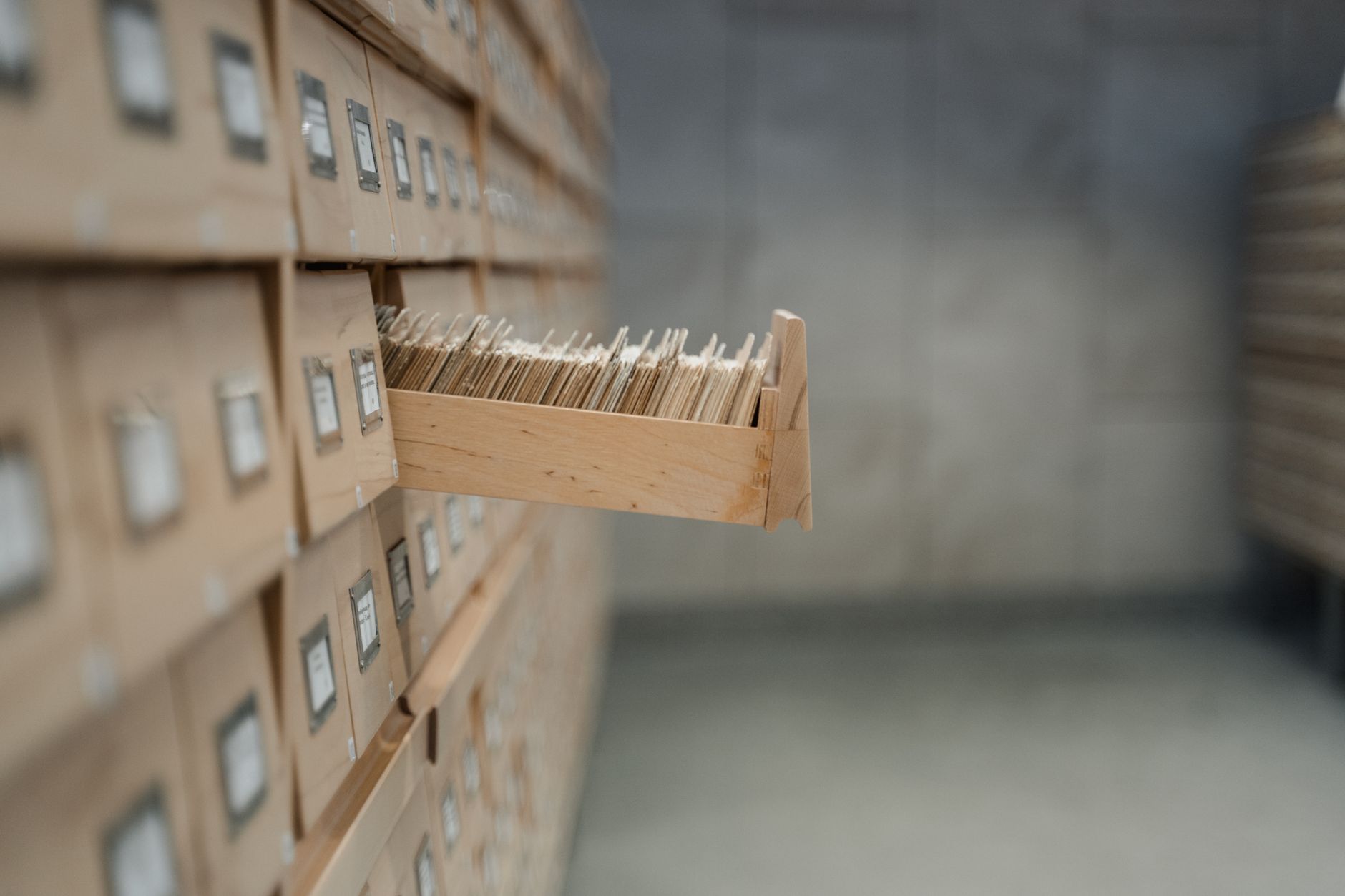 An open wooden card-catalogue drawer pulled out from a wall of labelled index drawers in an archive.